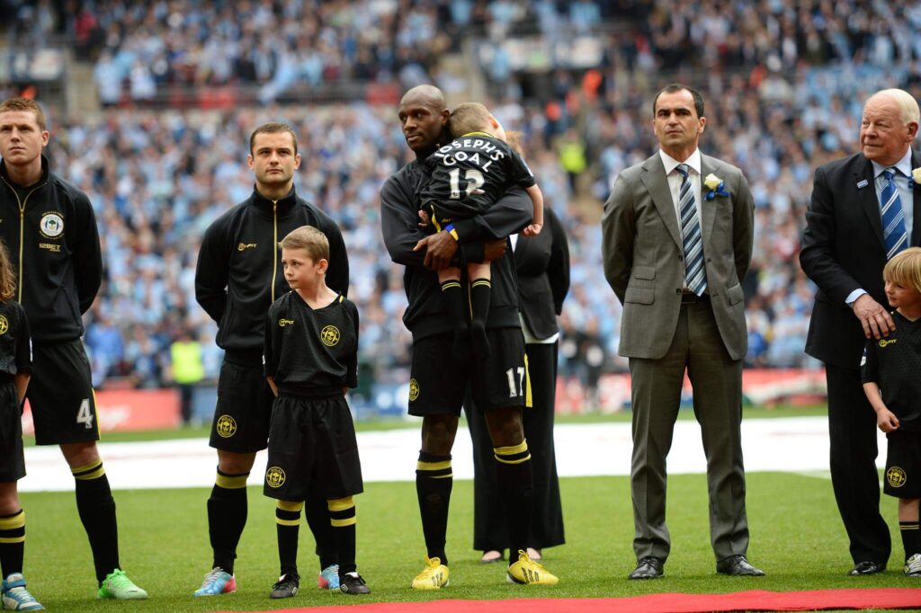 Football players stood on a field with one holding Joe from Josephs Goal in his arms