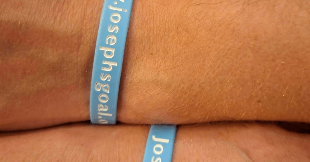 Close-up of a blue Joseph’s Goal wristband being worn around a person’s wrist.